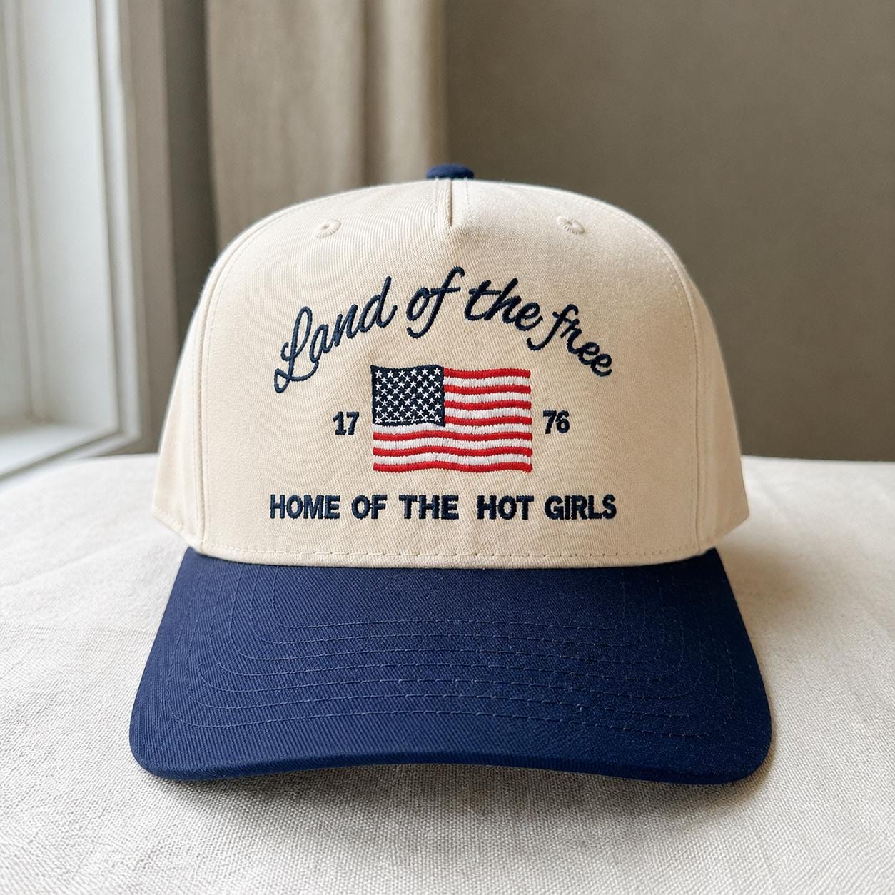 Cream and navy embroidered trucker hat with Land of the Free lettering and American flag motif