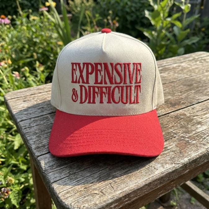 Front view of cream and red embroidered trucker hat resting on a wooden table