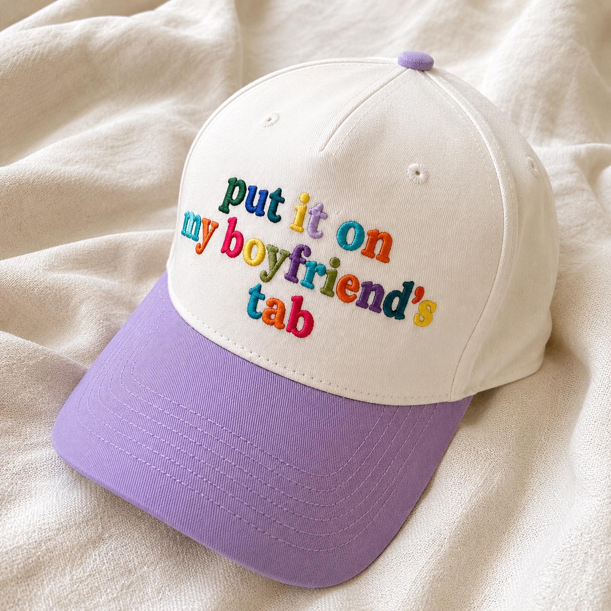 Two-tone cream and lavender hat with colorful embroidered “put it on my boyfriend’s tab” lettering