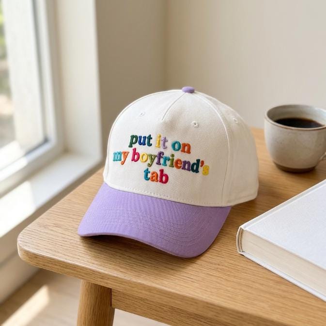 Two-tone embroidered hat displayed beside coffee and a book
