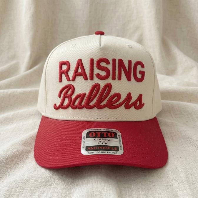 Front view of a cream and red Raising Ballers embroidered trucker hat
