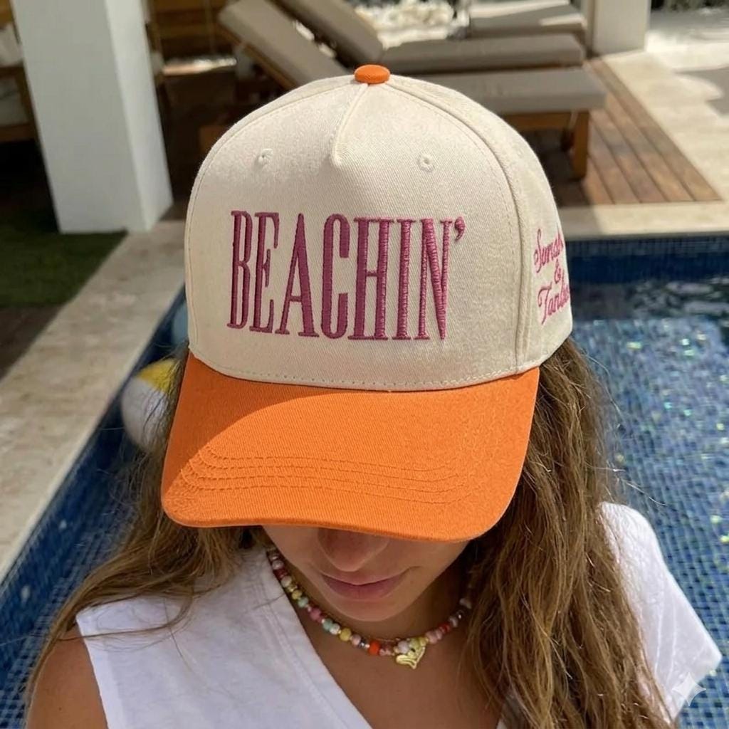 Person wearing a cream and orange Beachin' embroidered hat beside a pool