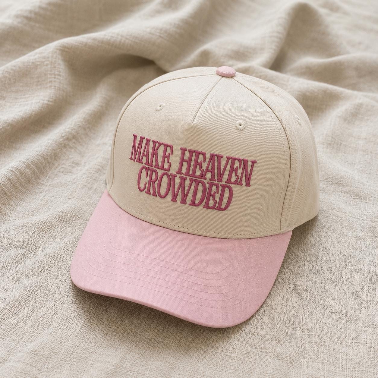 Two-tone cream and pink trucker hat embroidered with Make Heaven Crowded lettering