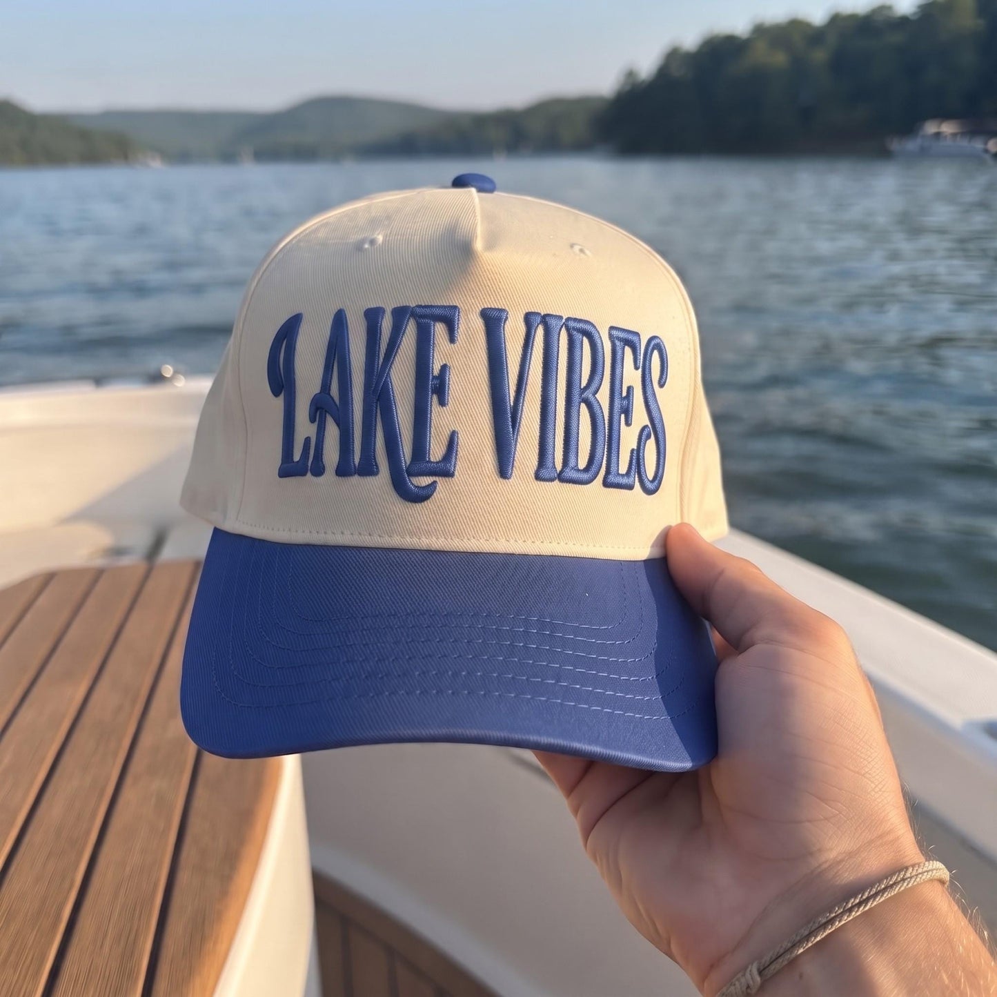 Embroidered Lake Vibes hat held beside a scenic lake
