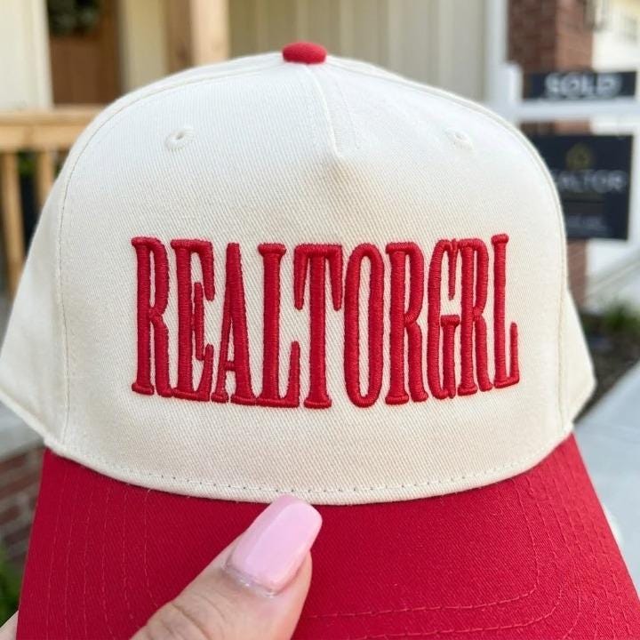 Close-up of red REALTORGRL embroidery on a cream cap