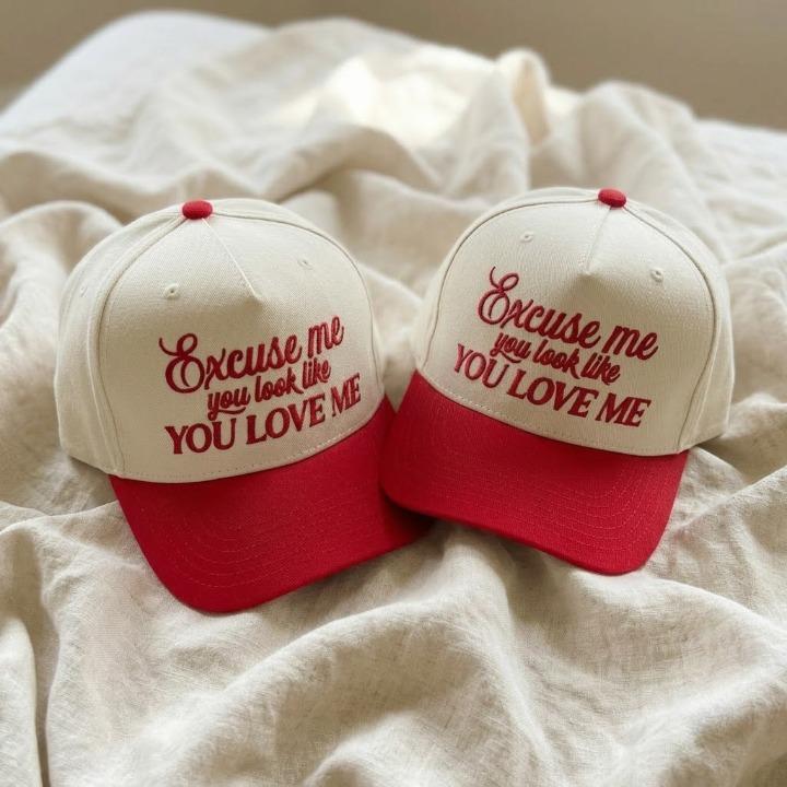 Two cream and red embroidered trucker caps displaying the phrase Excuse me, you look like you love me