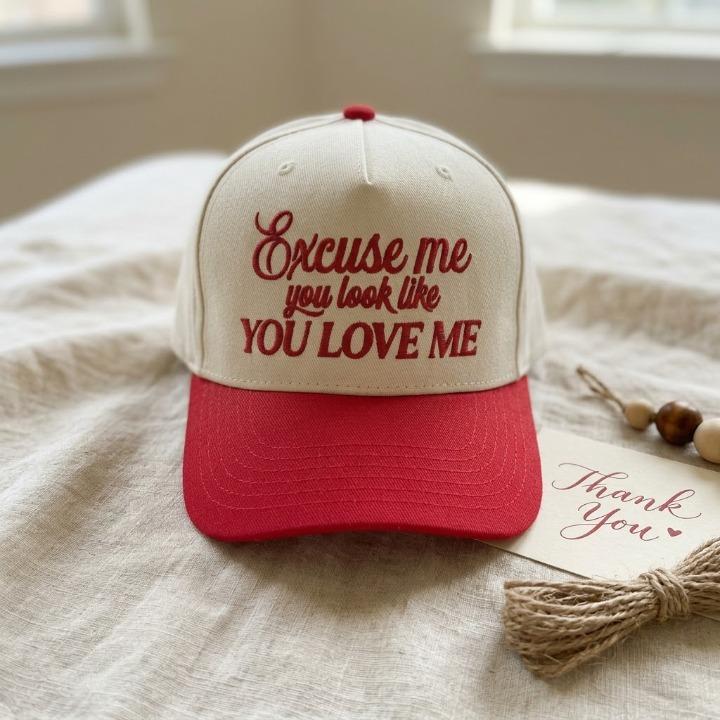 Front view of cream and red trucker cap with Excuse me you look like you love me lettering