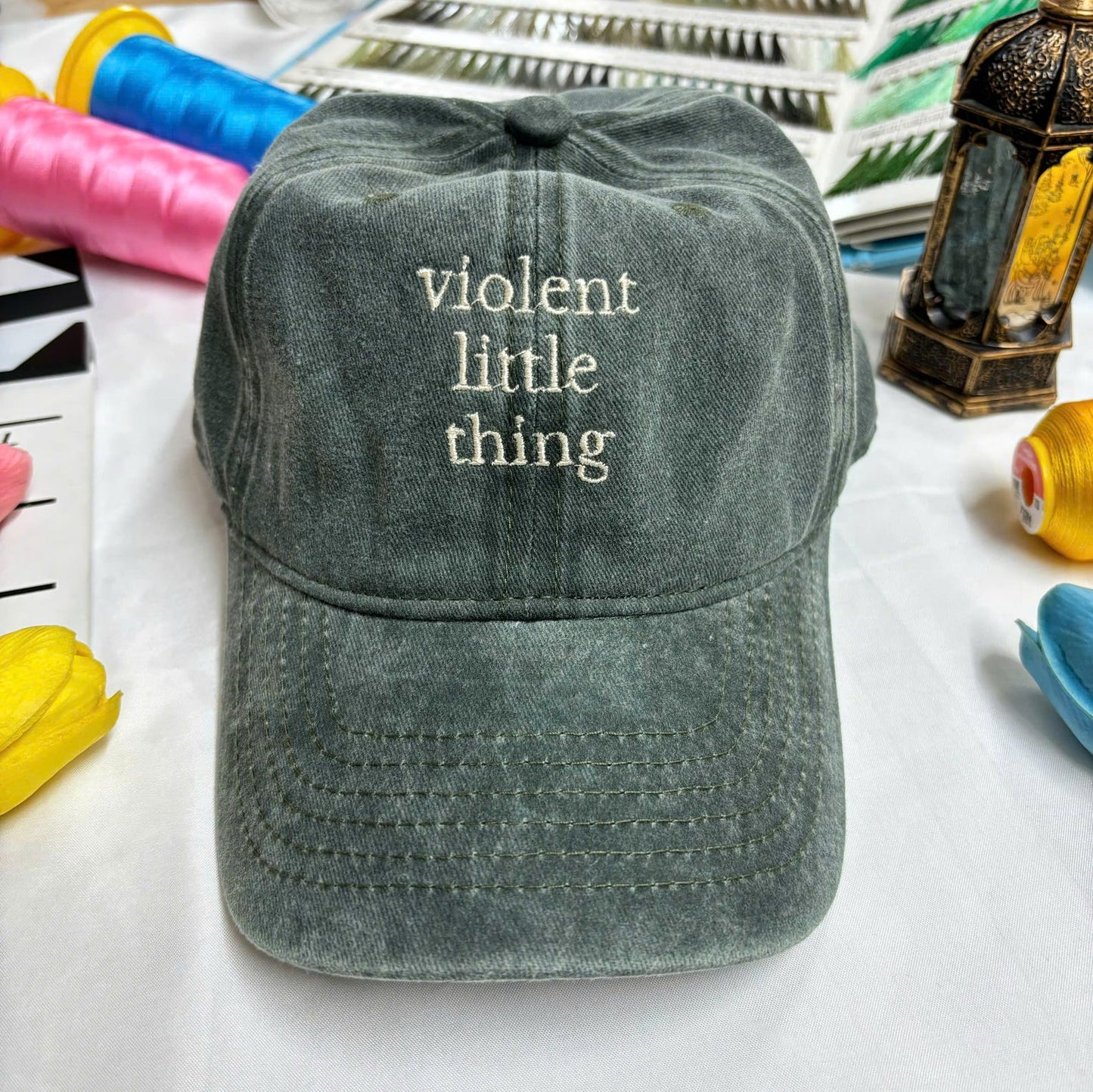 Washed dark green dad hat with embroidered quote “violent little thing” in off-white thread – minimalist and edgy fashion piece