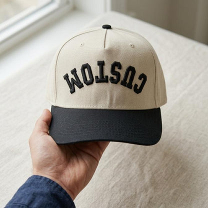 Front view of beige and black two-tone trucker hat with bold CUSTOM embroidery