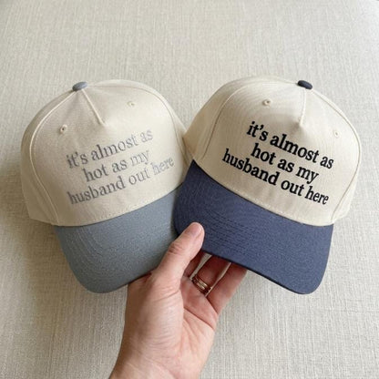 Two two-tone trucker hats embroidered with the phrase it’s almost as hot as my husband out here