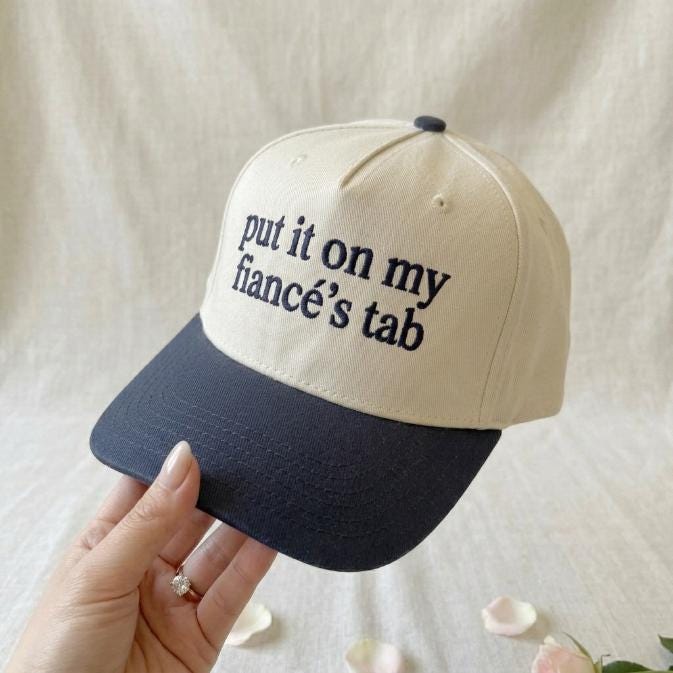 Front view of funny fiancé statement trucker hat in cream and navy