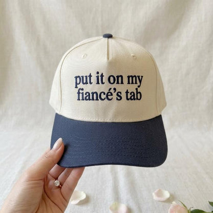 Two-tone cream and navy trucker hat with put it on my fiancé’s tab front text