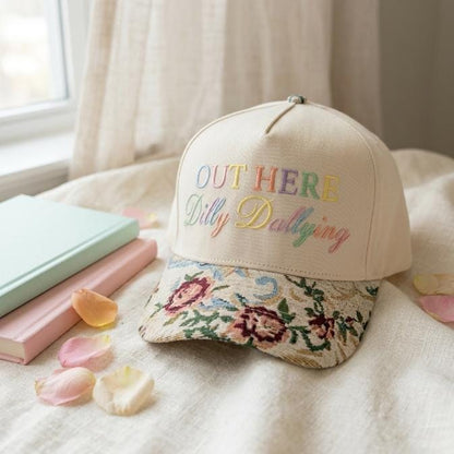 Floral embroidered hat resting on a bed beside pastel books and flower petals