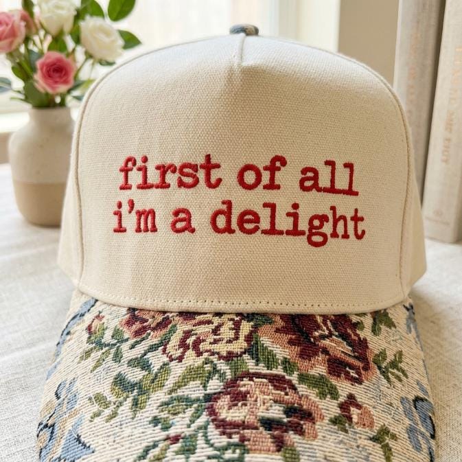 Close-up of red “first of all i’m a delight” embroidery above a floral-patterned brim
