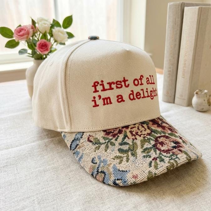 Three-quarter view of cream hat with floral patterned bill and embroidered message