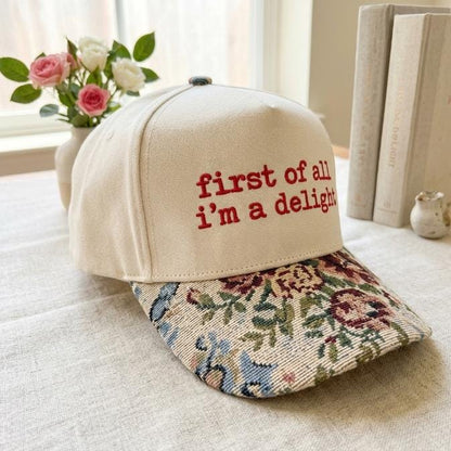 Three-quarter view of cream hat with floral patterned bill and embroidered message