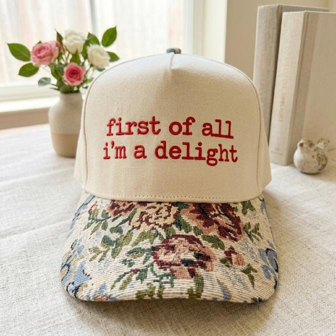 Cream statement hat showing red embroidered phrase and colorful floral brim