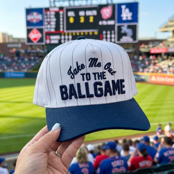 White pinstripe baseball hat with Take Me Out to the Ballgame embroidery at a baseball stadium