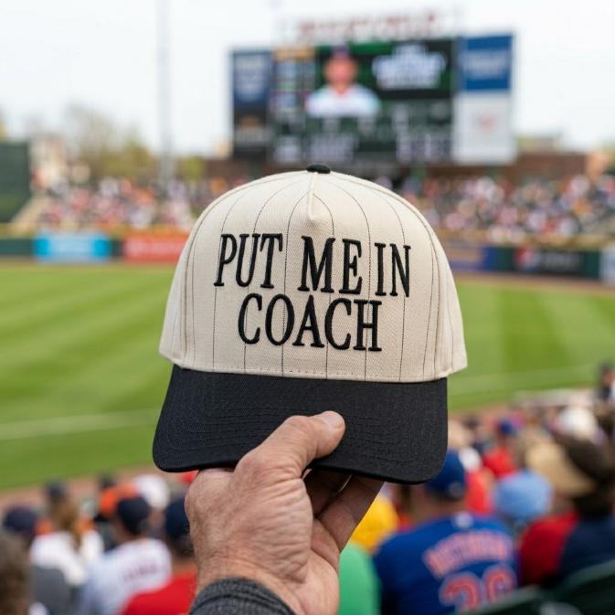 Put Me In Coach pinstripe baseball hat with black brim held at a baseball stadium
