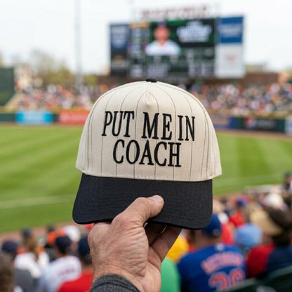 Put Me In Coach pinstripe baseball hat with black brim held at a baseball stadium