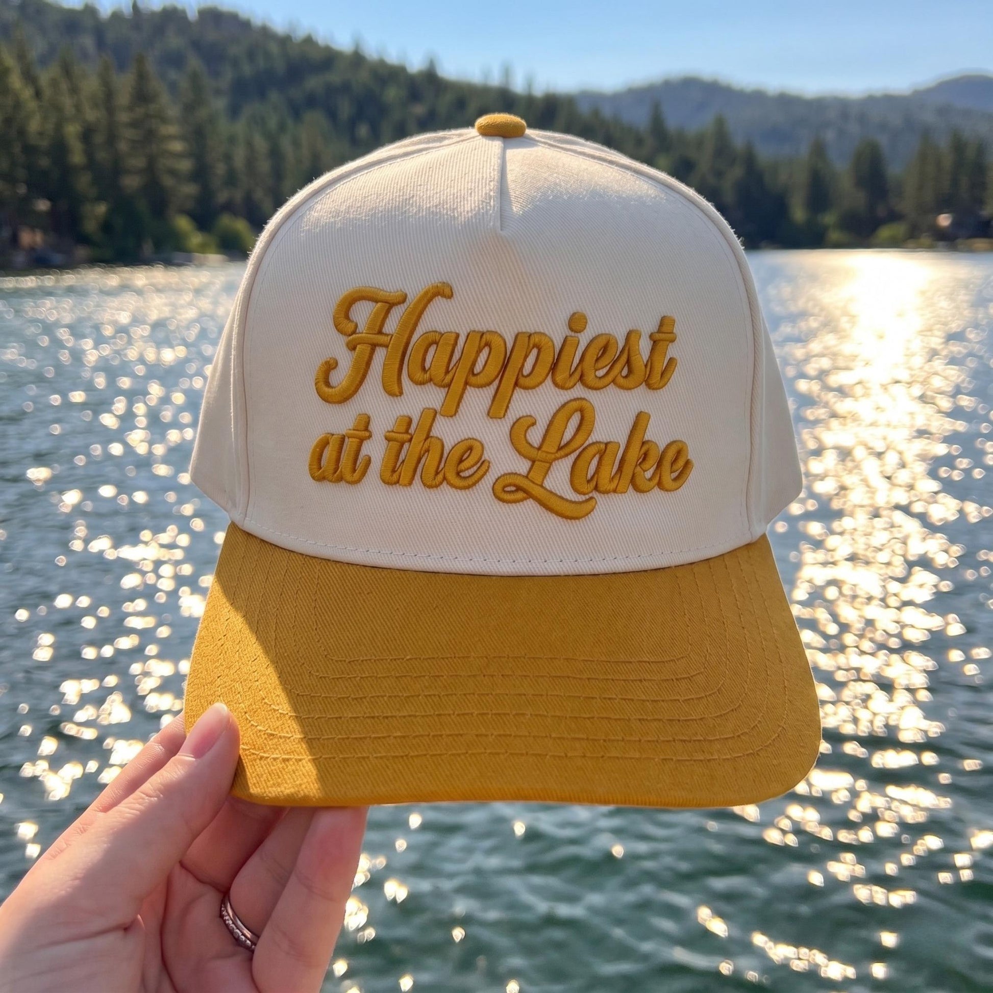 Cream and gold two-tone Happiest at the Lake embroidered hat by a scenic lake