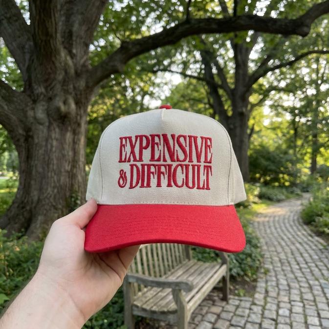 Two-tone cream and red trucker hat embroidered with “Expensive & Difficult” lettering