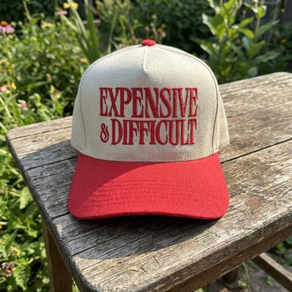 Front view of cream and red embroidered trucker hat resting on a wooden table