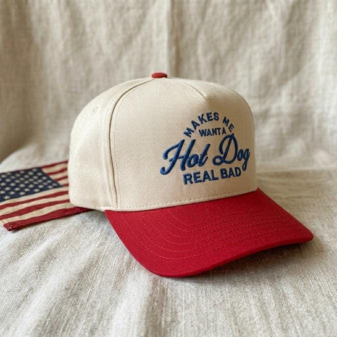 Angled view of two-tone trucker hat with blue embroidered hot dog lettering