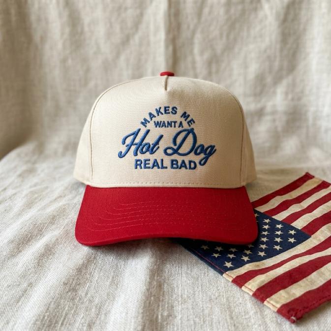 Cream and red hot dog embroidered trucker hat displayed with an American flag