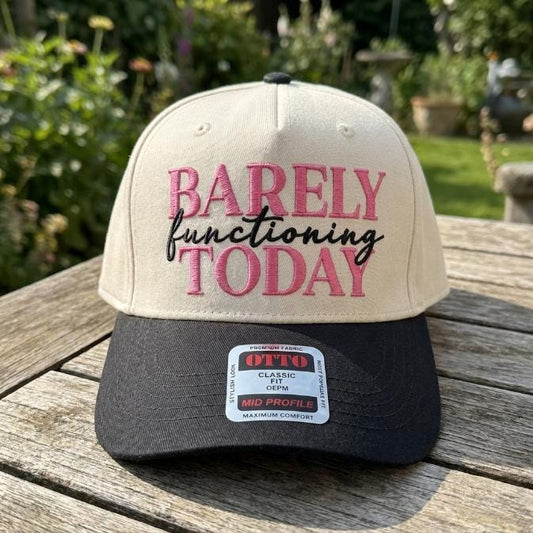 Two-tone cream and black trucker hat embroidered with Barely Functioning Today in pink and black lettering