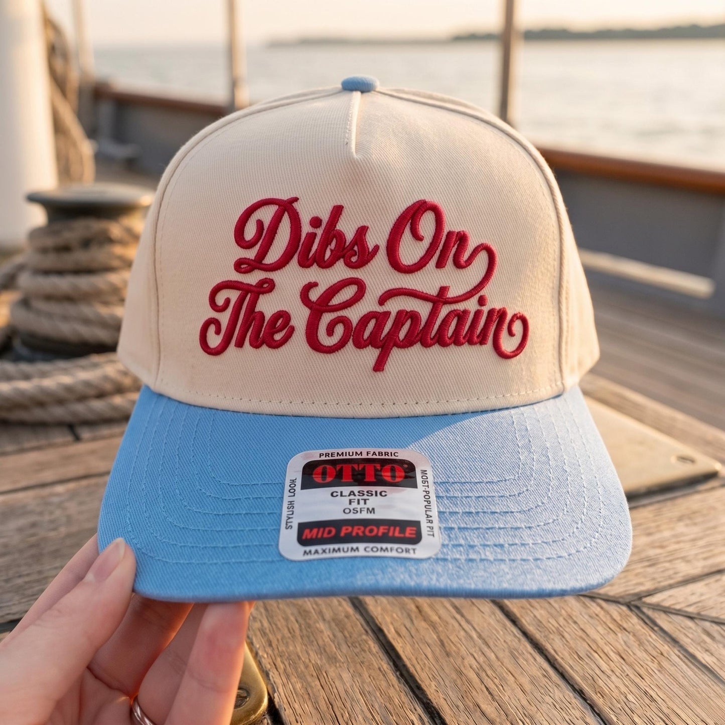 Dibs On The Captain hat shown with red script embroidery and a light blue brim