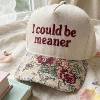 Cream embroidered hat with maroon “I could be meaner” lettering and floral-patterned brim