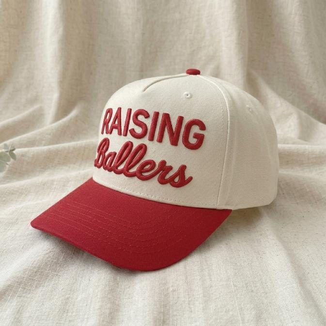 Angled view showing the raised lettering and red bill on the Raising Ballers hat