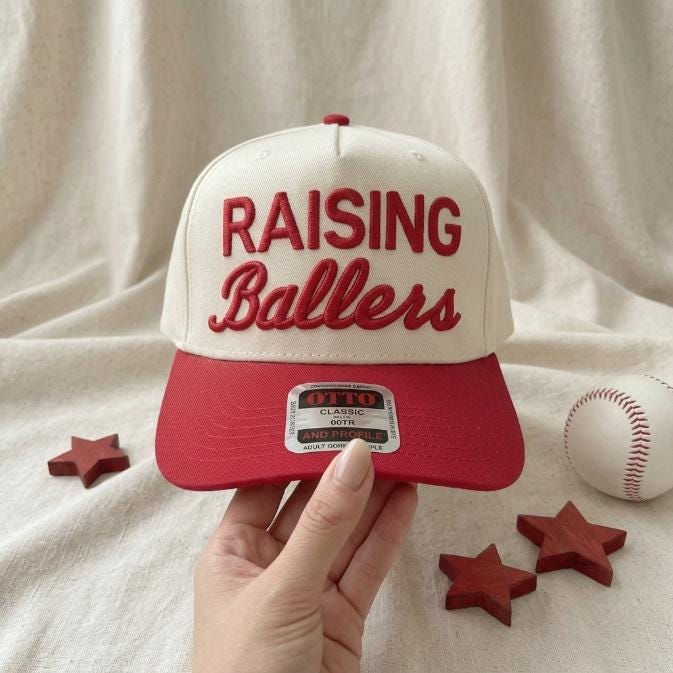 Raising Ballers two-tone hat held in hand with a baseball and decorative stars
