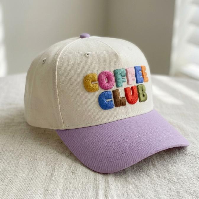 Angled view of cream and lavender embroidered Coffee Club cap
