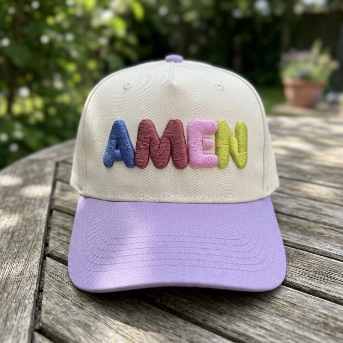Embroidered AMEN cap displayed outdoors on a wooden table