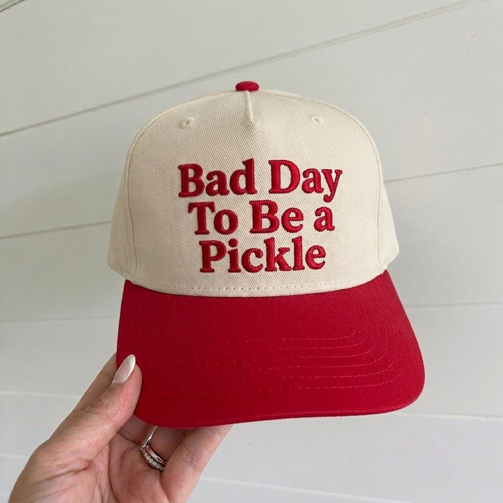 Cream and red two-tone trucker hat with “Bad Day To Be a Pickle” embroidered in red