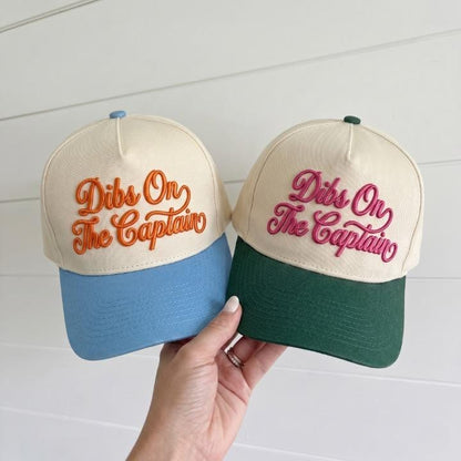 Two two-tone trucker hats embroidered with Dibs On The Captain in orange and pink thread