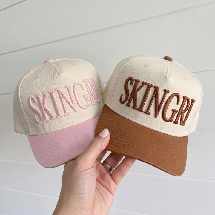 Two two-tone SKINGRL embroidered trucker caps in pink and brown color combinations