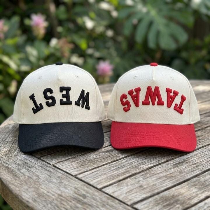 Two embroidered EAST and WEST trucker caps displayed on a wooden table
