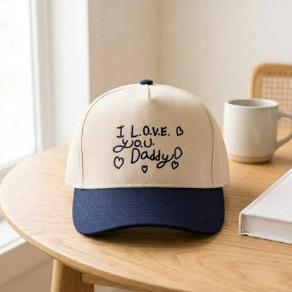 Two-tone cream and navy Daddy gift cap shown on a wooden table