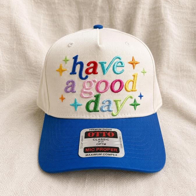 Front view of a colorful “have a good day” embroidered trucker cap on a light fabric background