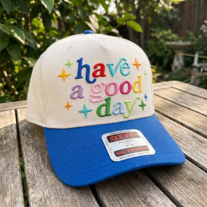 Angled view of a white and blue trucker hat with multicolor phrase and star embroidery