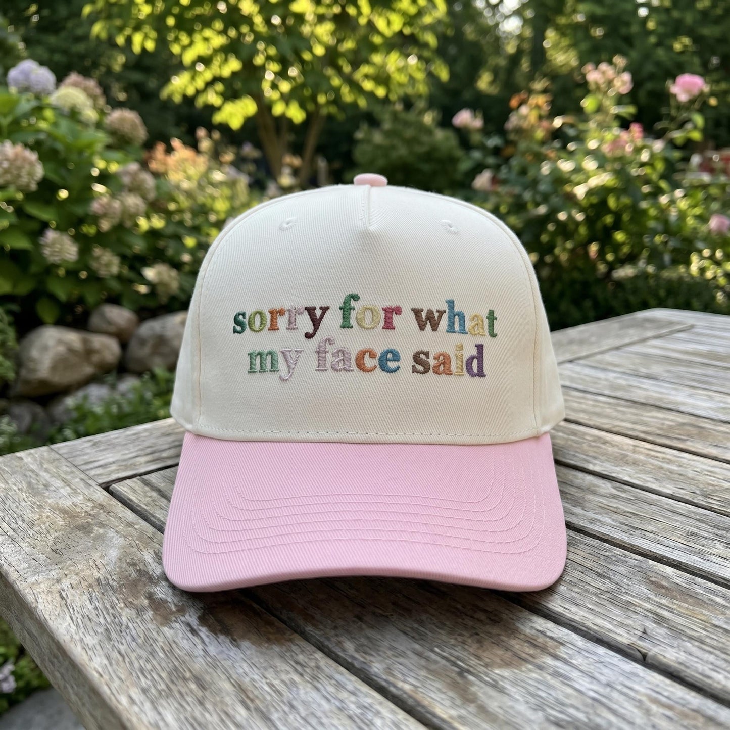 Embroidered sorry for what my face said trucker hat displayed outdoors on a wooden table