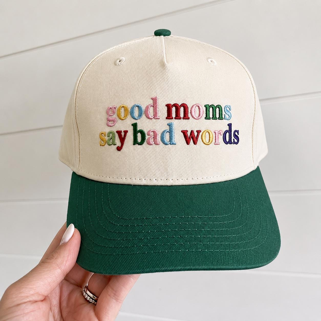 Two-tone cream and forest green trucker hat with multicolor “good moms say bad words” embroidery