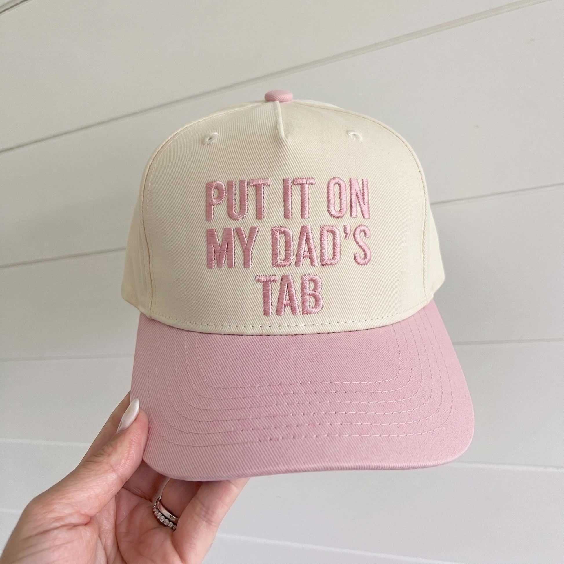 Two-tone cream and pink embroidered trucker hat reading Put It On My Dad's Tab