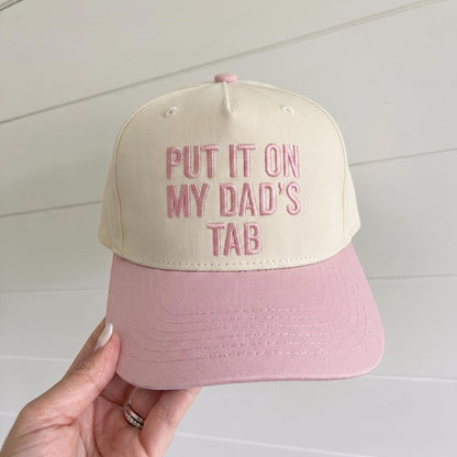 Two-tone cream and pink embroidered trucker hat reading Put It On My Dad's Tab