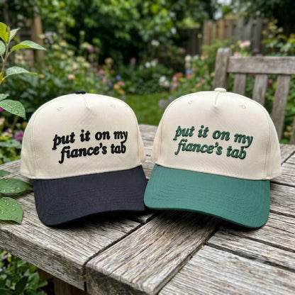 Black brim embroidered fiance's tab trucker hat held outdoors