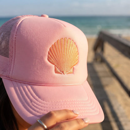 Close-up of pink trucker hat with orange seashell embroidery near a pier