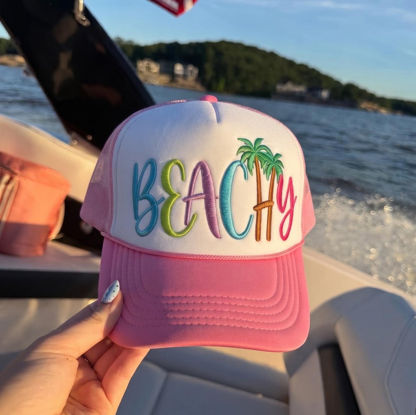 Pink and white beach trucker hat with colorful BEACH embroidery and palm trees on a boat